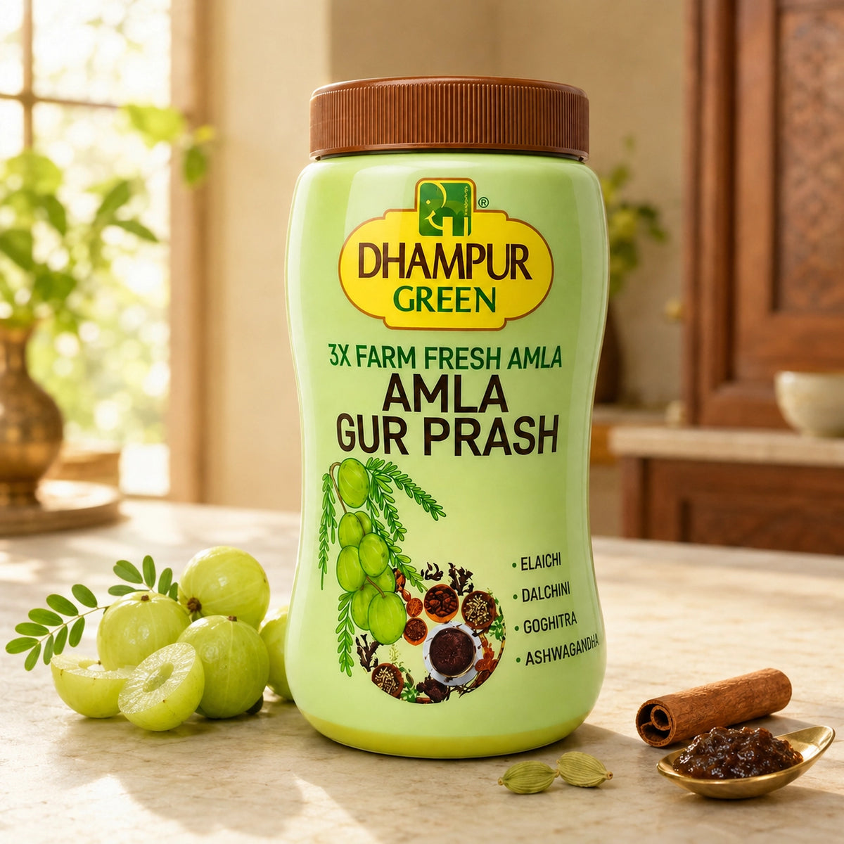 A jar of DHAMPUR GREEN Amla Gur Prash sits on a kitchen counter surrounded by fresh green amlas, a cinnamon stick, and cardamom seeds. The background shows a warm, sunlit kitchen interior.
