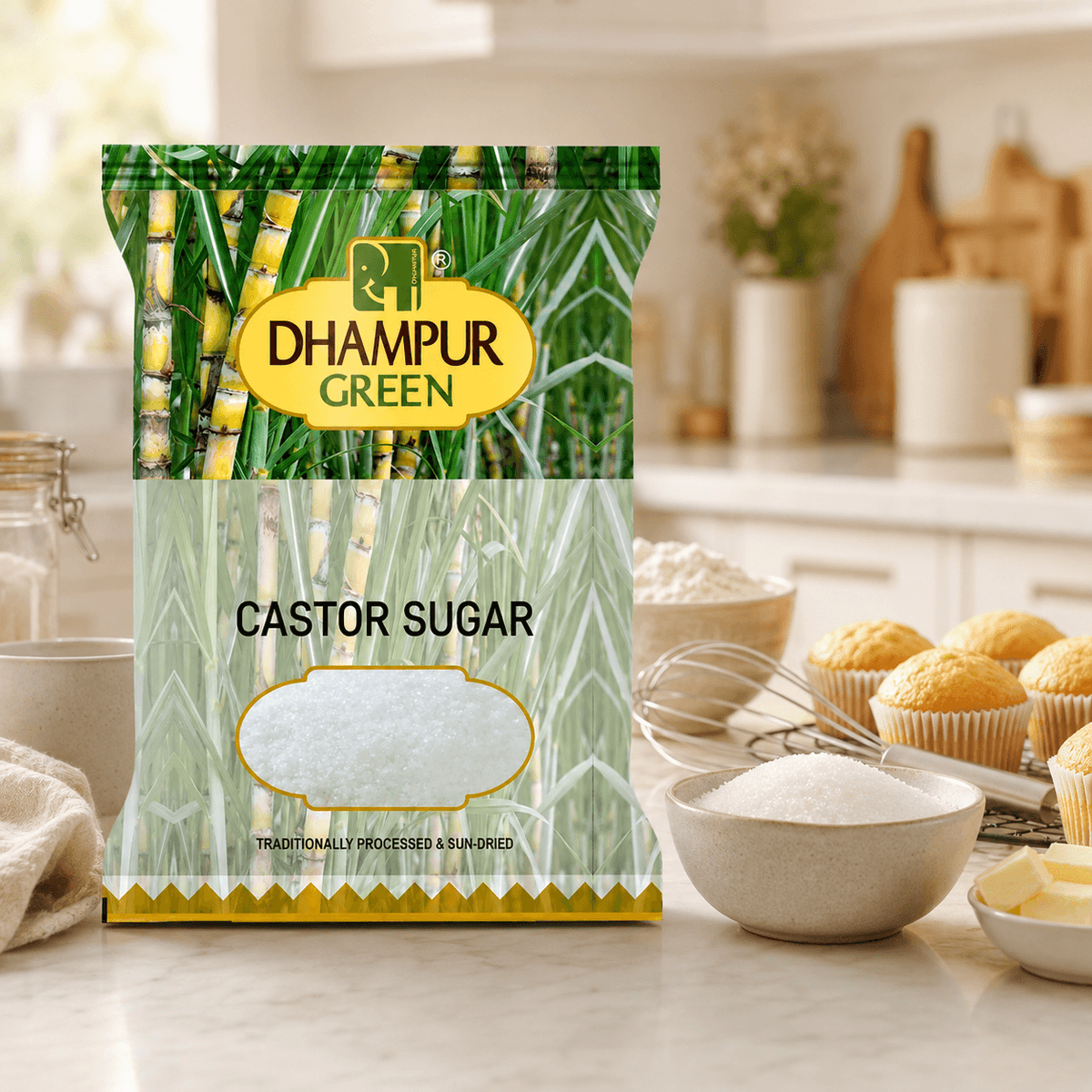 A bag of Dhampur Green Castor Sugar stands on a kitchen counter with baking ingredients and cupcakes nearby, in a bright, softly blurred kitchen setting.