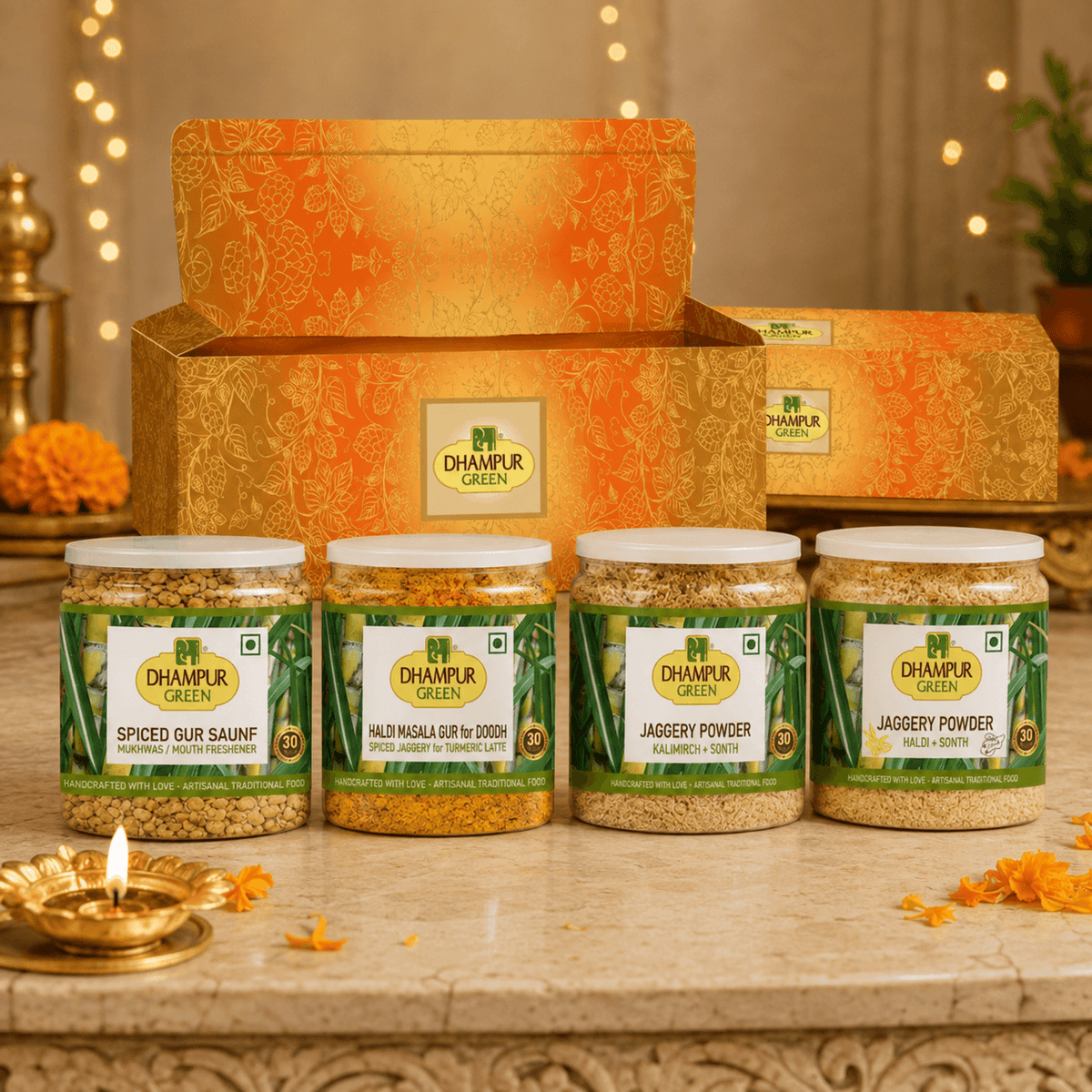A Dhampur Green gift set containing four jars of spices (Gur Saunf, Jaggery Powder, Malai Chutney, and Phalodi Masala Guri) arranged on top of an orange patterned box.