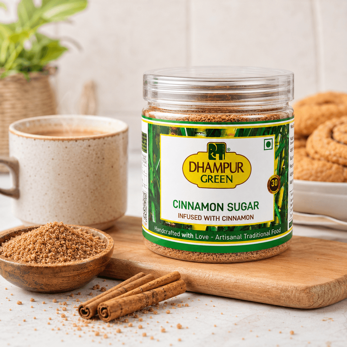 A jar of Dhampur Green Cinnamon Sugar sits on a wooden board with cinnamon sticks, a small bowl of brown sugar, and a mug in a warm kitchen setting.