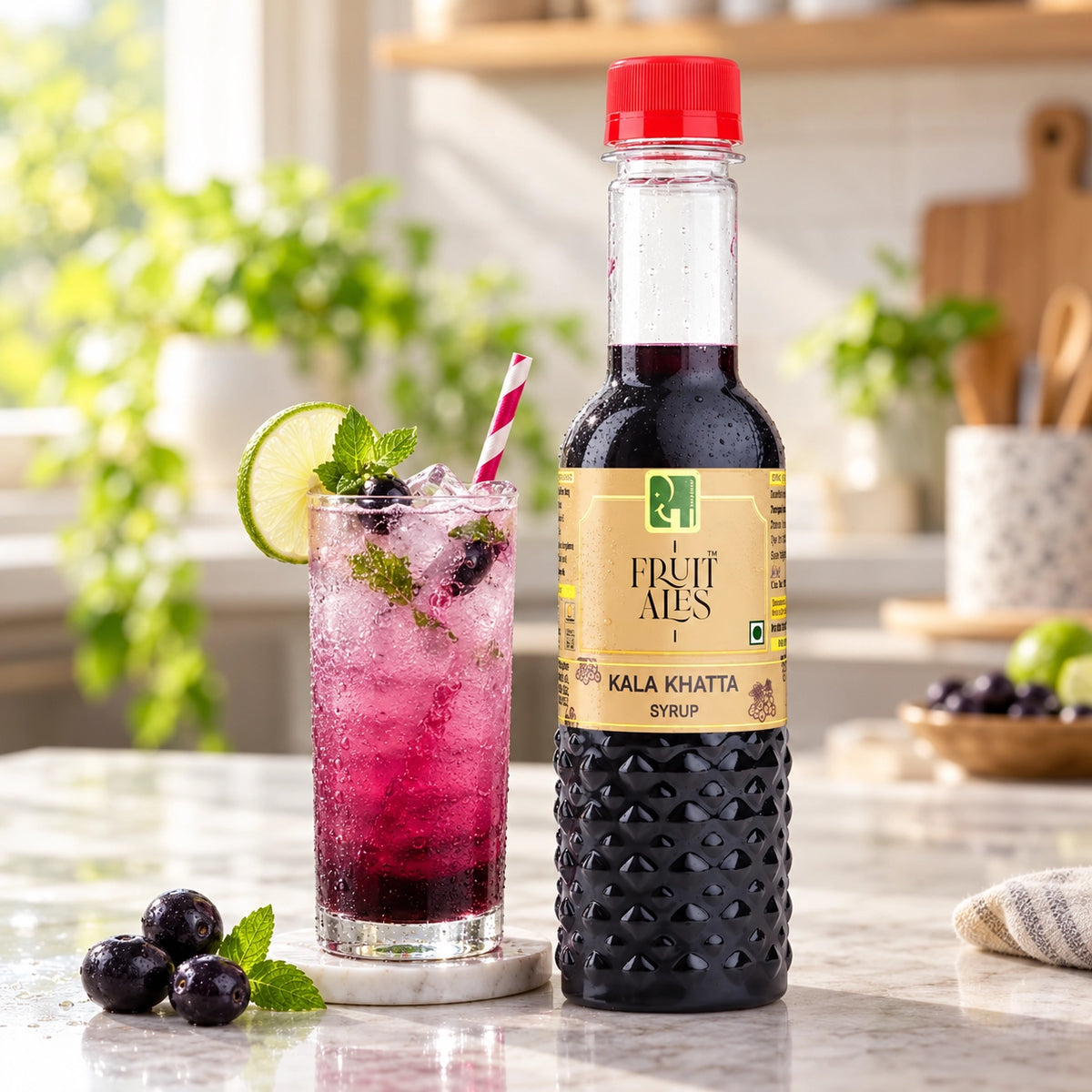 A bottle of FRUIT ALES KALA KHATTA SYRUP stands on a marble countertop next to a tall glass of pink berry drink garnished with a lime wheel, mint, and blueberries in a bright kitchen setting.
